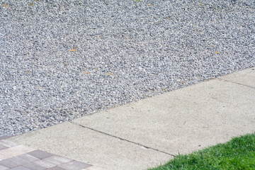 Close-up view of gravel and concrete pavement with green grass. Ideal for landscaping projects or...