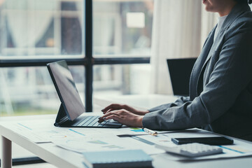 Businesswoman Focused on Laptop: A confident business woman in a professional suit sits at her desk, intently focused on her laptop, surrounded by paperwork and a calculator, showcasing the dedication