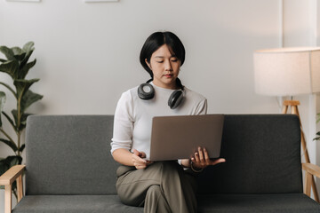 Focused on the Task: A woman in a modern home setting, engrossed in work on her laptop while...