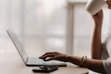 Focused Flow: Woman typing on laptop while sipping coffee, bathed in natural light, evoking a sense of productivity and calm.
