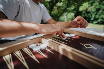 Close-up of a person enjoying a game of backgammon outdoors. The scene captures the strategic game...