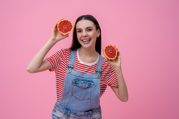 Cute smiling young woman holding slices of grapefruit in hands