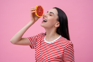Pretty happy young woman in striped tshirt with part of grapefruit in hand