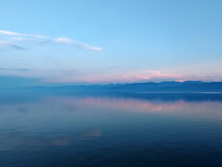 Silhouette of mountains near lake at evening with pink clouds and sky