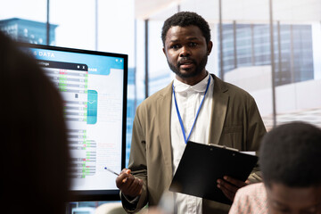 Fototapeta premium Financial expert briefing his team members about new enterprise objectives, showing analysis of their budget and expenses on interactive board. Resource allocation and project planning meeting.