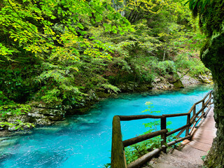 A serene turquoise river winding through a rocky gorge with a wooden walkway along the cliff