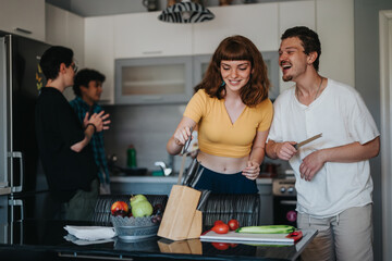 A group of friends happily cooking together in a contemporary kitchen. They are preparing fresh...