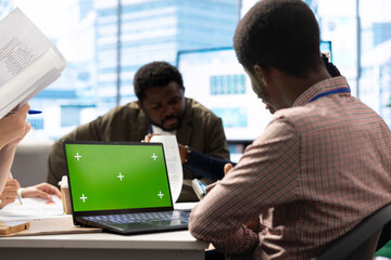 Diverse team of employees using mockup copy space screen on gadget, discussing ways to increase the company budget. Business experts preparing for a presentation in a boardroom meeting.