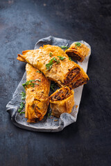 Traditional Turkish crispy sigara borek rolls with minced meat rolled in fillo pastry served as close-up in a Nordic design tray on a black board
