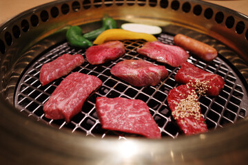 A close-up shot of premium Wagyu beef slices grilling on a traditional Japanese Yakiniku barbecue.