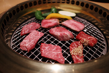 A close-up shot of premium Wagyu beef slices grilling on a traditional Japanese Yakiniku barbecue.