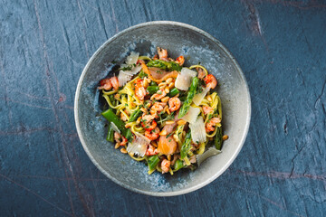 Traditional Italian Pasta with green Green asparagus, prawns and smoked salmon slices served with pine nuts and parmesan cheese slices as top view in a Nordic design bowl