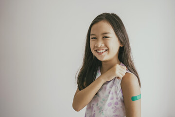 Mixed Asian preteen girl showing her arm with bandage after got vaccinated or inoculation, child...