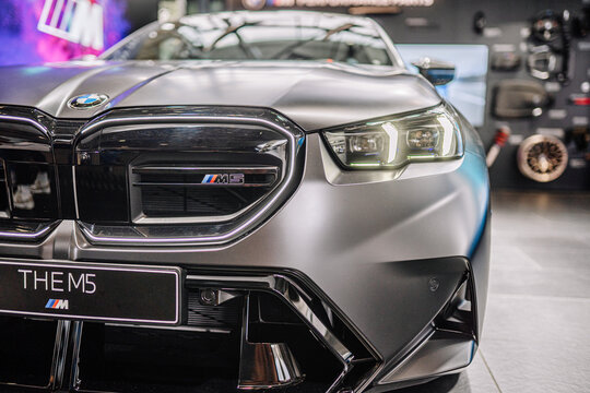 Munich, Germany - September 13, 2024 - Close-up of the front of a matte black BMW M5, highlighting the grille, headlights, and sleek design in a showroom with reflections.