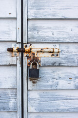 Rusty padlock and latch on white aged weathered closed wooden door. Closeup of rusted metal lock and old vintage rustic texture.  Shabby chic design. Security safety and industrial concept. Copy space