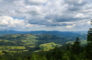 Summer landscape with village houses are scattered at the mountain hills are lush with greenery and trees under a clear blue sky with scattered clouds. Carpathian Mountains, Ukraine