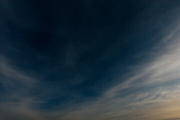 A serene, expansive lake reflects the soft glow of a starry night sky. Wispy clouds stretch across...