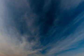 A serene, expansive lake reflects the soft glow of a starry night sky. Wispy clouds stretch across the horizon, adding to the calm, tranquil atmosphere. The distant shoreline is faintly visible