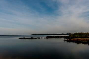 Fototapeta premium A tranquil lake at dusk, with small boats lined along the shore. The smooth water reflects the evening sky, filled with soft clouds and a few stars. The calm atmosphere creates a peaceful