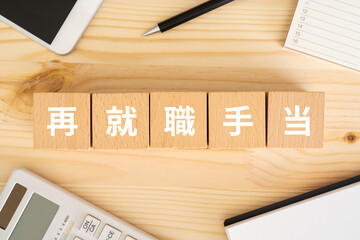 再就職手当の文字が入ったブロック、電卓、スマホ、ノート