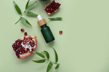 Composition with bottle of essential oil, pomegranate and plant leaves on green background