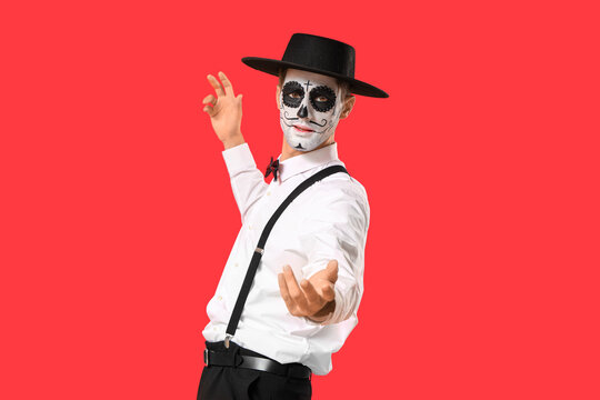 Young man with painted skull on red background. Mexico's Day of the Dead (El Dia de Muertos) celebration