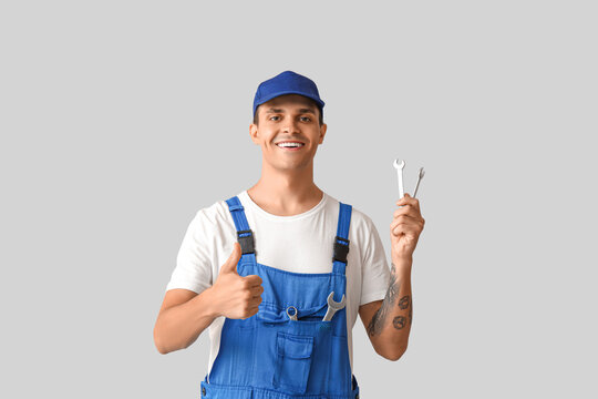 Male car mechanic with wrenches showing thumb-up on grey background