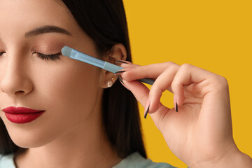 Obraz premium Beautiful young woman applying stylish eyeshadows on yellow background