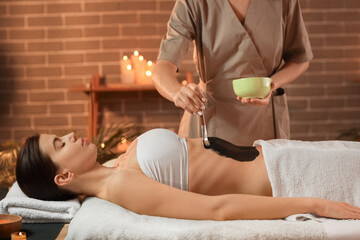 Massage therapist applying mud on woman's belly in dark spa salon