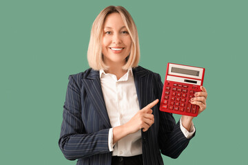 Mature female math teacher pointing at calculator on green background