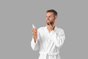 Handsome young man with cosmetics for beard on grey background