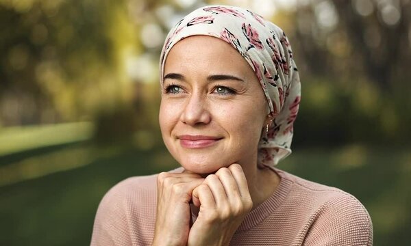 A young woman wearing a scarf on her head, indicative of chemotherapy, with a determined and hopeful look in her eyes