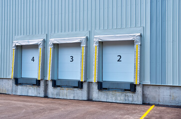 Side view of a building with three industrial loading docks. Each dock has a closed blue roll-up door and is equipped with an extendable dock leveler at the base.
