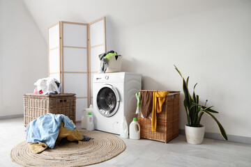 Interior of light bathroom with washing machine, pile of dirty clothes and laundry basket