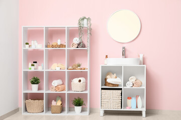 Shelving unit with sink, mirror and bath accessories near pink wall in room