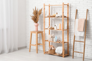 Modern shelving unit with bath accessories, pampas grass and ladder near white brick wall in room