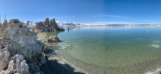 An extreme wide shot capturing the serene waters of Mono Lake on a calm, clear day. The lake's...