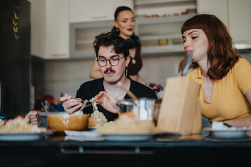 A group of friends sharing a meal in a cozy kitchen setting, highlighting camaraderie and casual dining. The scene reflects warmth, connection, and relaxed conversation over food.