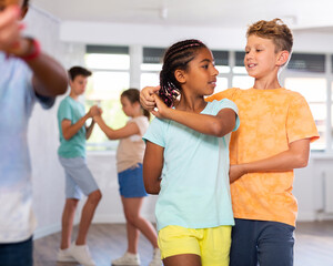 Group of positive juvenile boys and girls doing Tango poses in training room during workout session
