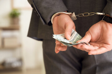 Handcuffed businessman with bribe in office, back view. Corruption concept