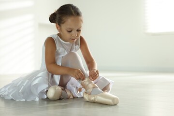 Little ballerina tying pointe shoes indoors, space for text