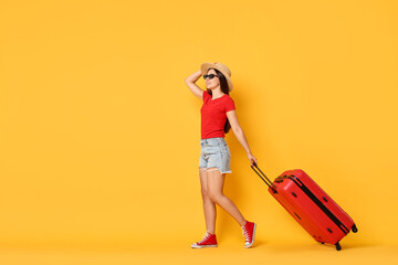 Happy young woman in sunglasses with suitcase on orange background