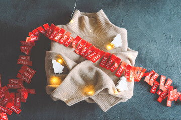 A soft, beige sweater is surrounded by bright red sale tags and glowing lights, creating a festive...