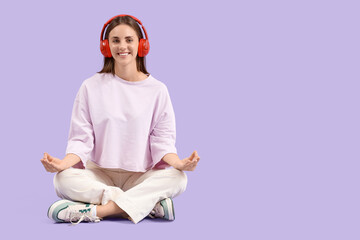 Young woman in headphones meditating on lilac background