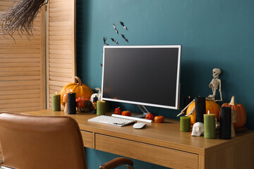 Workplace with blank computer monitor and Halloween decor near blue wall in office