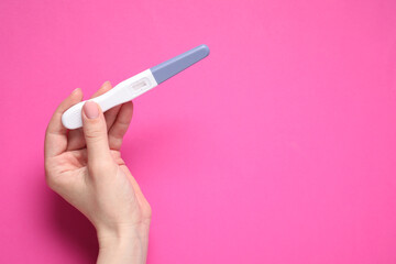 Woman holding pregnancy test on pink background, top view. Space for text