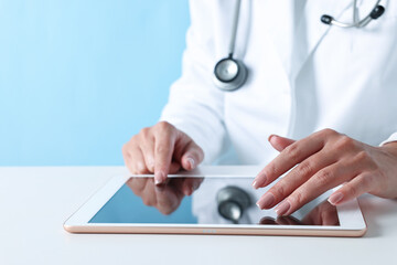 Doctor with tablet at table against light blue background, closeup view