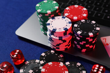 Poker chips, laptop and dices on blue table. Online game