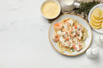 Tasty pasta with shrimps, creamy sauce and cheese served on white marble table, flat lay. Space for text