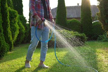 Man watering green grass on lawn in backyard, closeup
